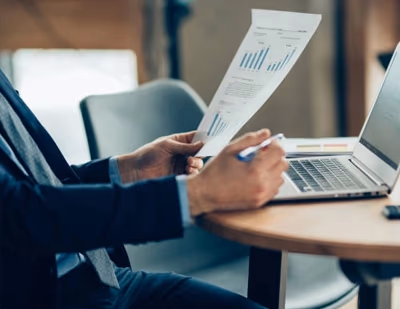 Persona analizando un informe financiero junto a un portátil